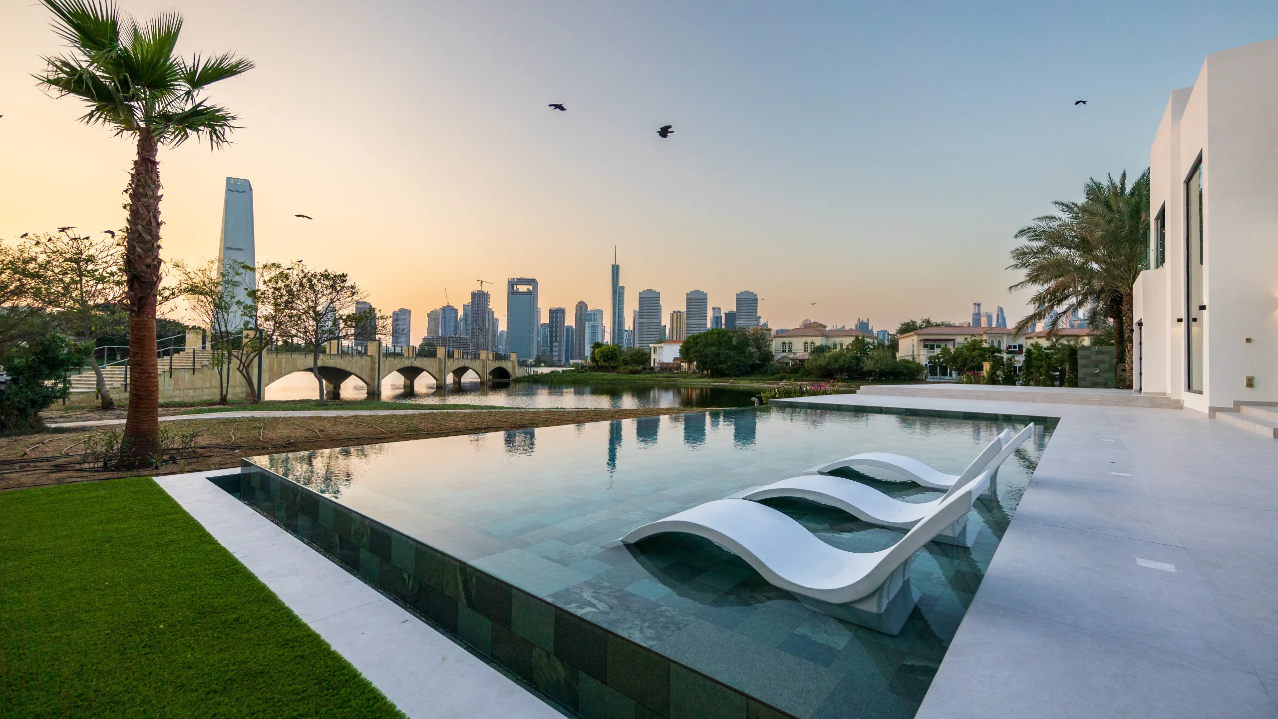 Sunloungers in a Jumeirah Islands swimming pool as the sun sets behind the Dubai skyline